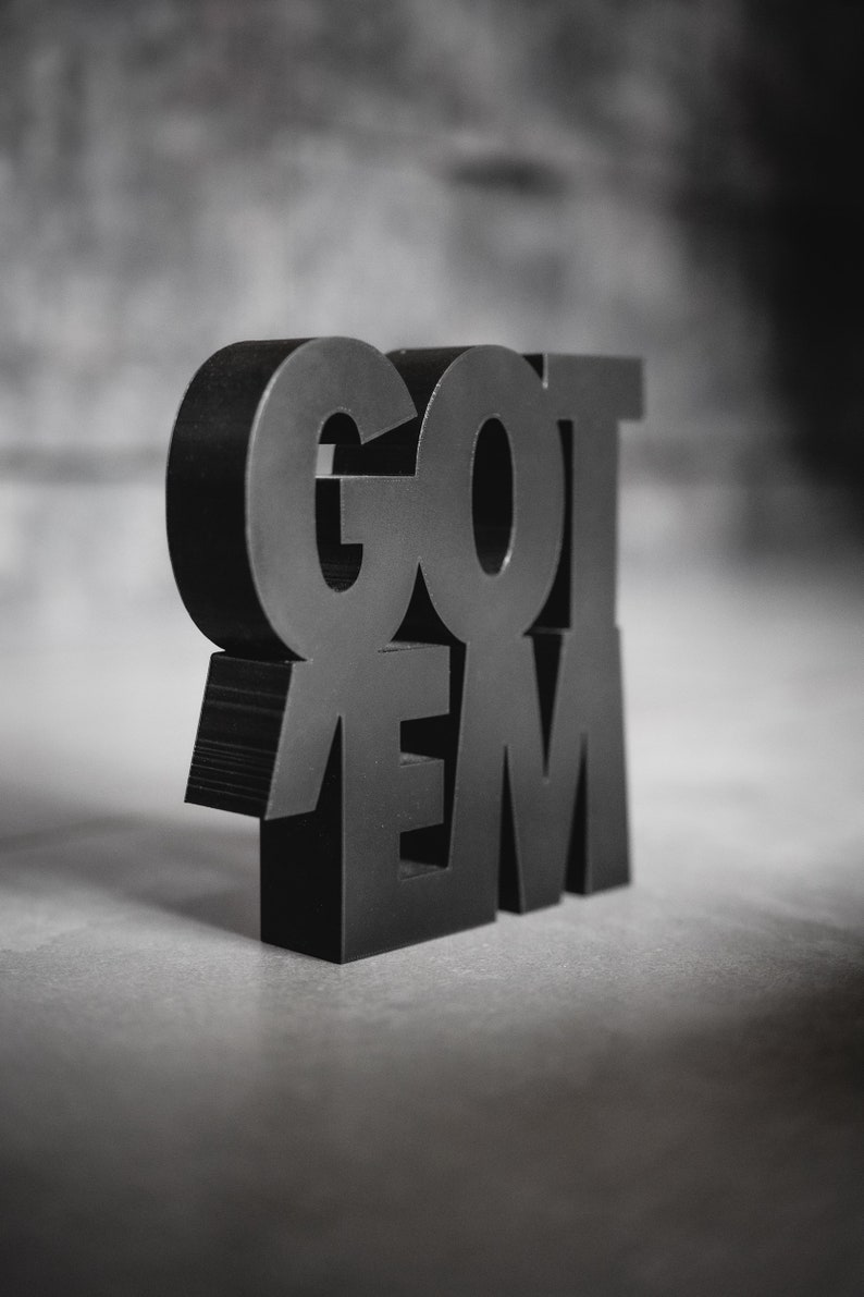 Peut inclure: Une enseigne en 3D imprim&eacute;e en noir avec les mots "GOT 'EM" en lettres grasses.