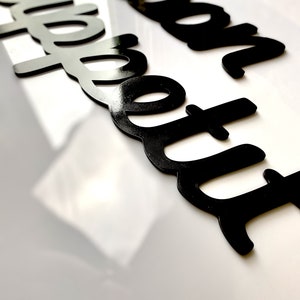 May include: Black acrylic letters spelling out "bon appetit" on a white surface.