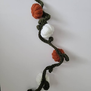 May include: A crocheted garland with alternating orange and white pumpkins and green leaves.