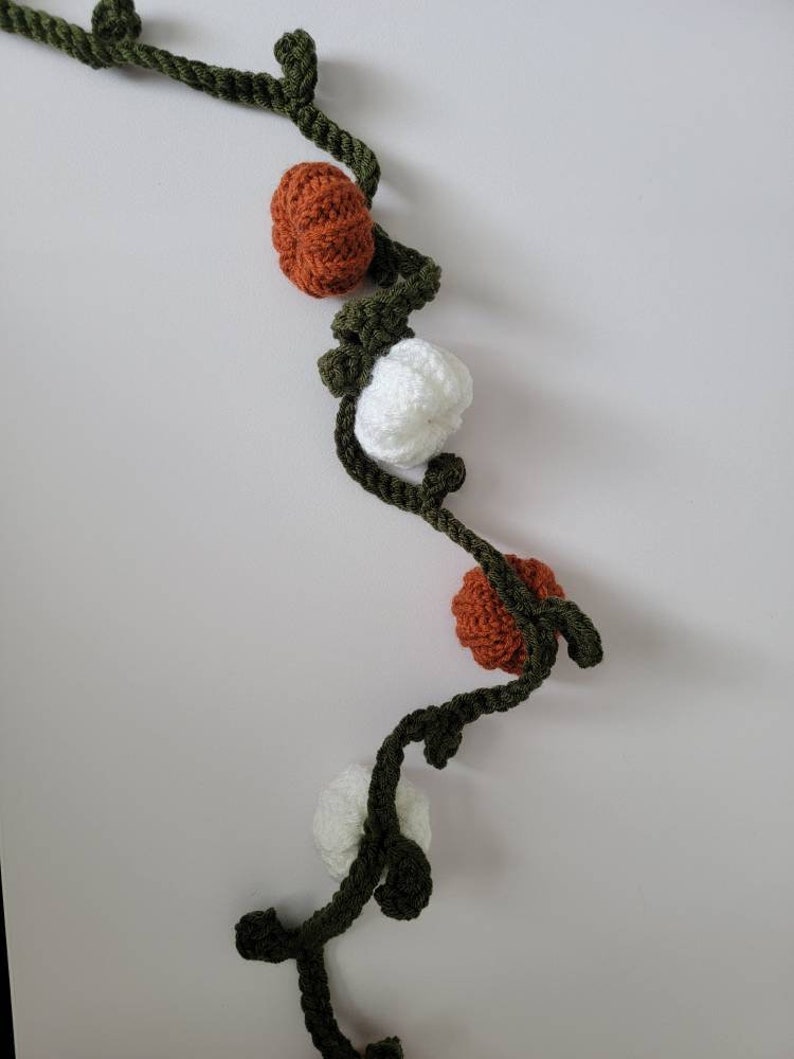 May include: A crocheted garland with alternating orange and white pumpkins and green leaves.