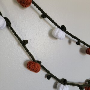 May include: A green garland with crocheted orange and white pumpkins. The garland is perfect for fall decor.