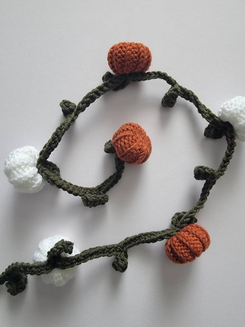May include: A crocheted garland with white and orange pumpkins and green leaves.