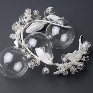 Peut inclure: Un accessoire de t&ecirc;te d&eacute;coratif compos&eacute; de fleurs de muguet en verre transparent et de feuilles blanches fix&eacute;es sur une armature en fil m&eacute;tallique souple, entrelac&eacute; avec trois sph&egrave;res en verre transparent de tailles diff&eacute;rentes.