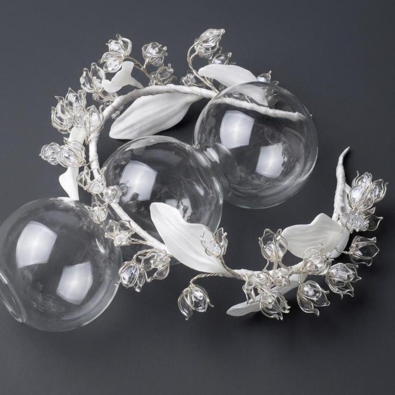 Peut inclure: Un accessoire de t&ecirc;te d&eacute;coratif compos&eacute; de fleurs de muguet en verre transparent et de feuilles blanches fix&eacute;es sur une armature en fil m&eacute;tallique souple, entrelac&eacute; avec trois sph&egrave;res en verre transparent de tailles diff&eacute;rentes.