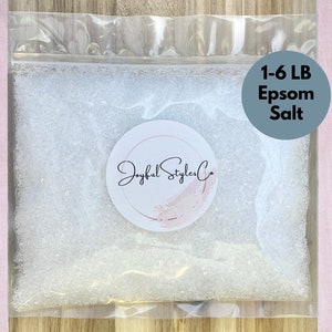 Puede incluir: Una bolsa de plástico transparente llena de sal de Epsom blanca. La bolsa tiene una pegatina con el texto "Joyful Styler Co" y un círculo azul con "1-6 LB Epsom Salt". El fondo es una tela rosa claro.