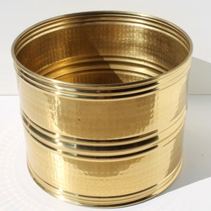 May include: A gold hammered metal planter with a round shape and two decorative bands around the rim.