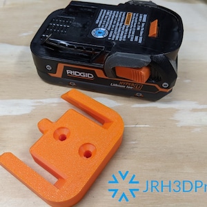 K&ouml;nnte beinhalten: Orangefarbener 3D-gedruckter Batteriehalter f&uuml;r einen Ridgid Hyper Li Lithium-Ionen-Akku. Der Halter hat drei L&ouml;cher f&uuml;r Montageschrauben.