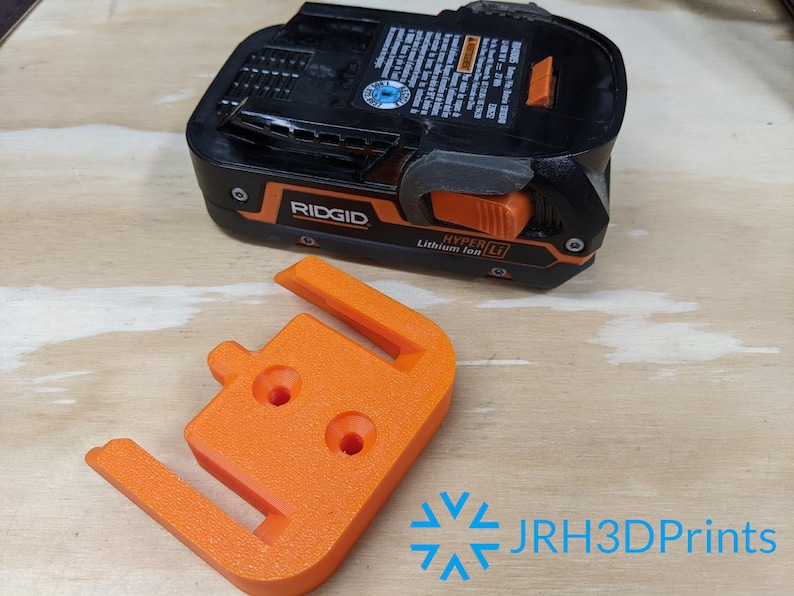 K&ouml;nnte beinhalten: Orangefarbener 3D-gedruckter Batteriehalter f&uuml;r einen Ridgid Hyper Li Lithium-Ionen-Akku. Der Halter hat drei L&ouml;cher f&uuml;r Montageschrauben.