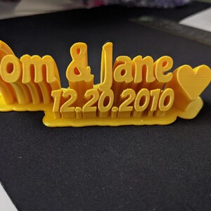 May include: A yellow 3D printed sign with the text "Tom & Jane 12.20.2010" and a heart.