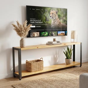 Peut inclure: Salon moderne avec une grande télévision affichant un documentaire animalier. En dessous, une console en bois avec des pieds en métal noir accueille des objets décoratifs et une plante en pot. Un canapé d'angle clair et un tapis complètent l'ensemble.
