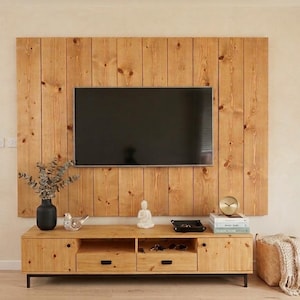 Può includere: Un televisore a schermo piatto montato su un pannello a parete composto da assi di legno marrone chiaro, sopra un mobile multimediale abbinato. Il mobile presenta due cassetti, due ripiani aperti e due armadietti laterali con maniglie nere.