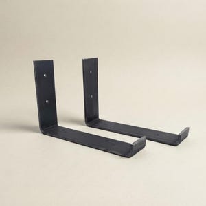 Pode incluir: Dois suportes de prateleira de metal em forma de L com acabamento em cinza carvão escuro. Cada suporte apresenta uma base horizontal plana com uma pequena borda virada para cima na extremidade e uma placa vertical com dois furos.