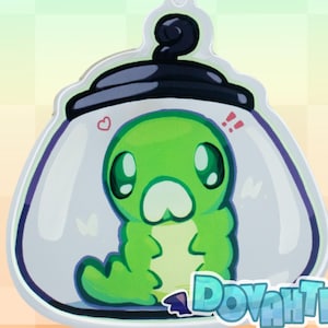 Op de afbeelding: Een heldere acryl sleutelhanger met een groene cartoonrups in een pot. De pot heeft een zwart deksel en een limoengroene sluiting. De rups heeft grote ogen en is omgeven door hartjes en uitroeptekens. De tekst "Dovahting" staat onderaan.