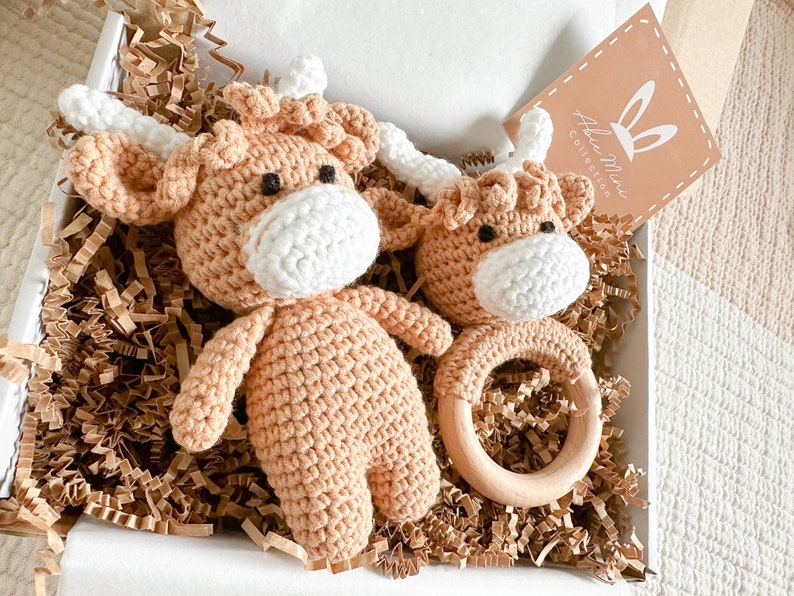 Peut inclure: Une bo&icirc;te cadeau remplie de papier de soie brun contient deux jouets en crochet en forme de vache Highland marron et blanche. L'un est un plus grand jouet en peluche et l'autre est un plus petit jouet &agrave; hochet avec un anneau en bois. La bo&icirc;te contient &eacute;galement une petite carte avec le texte "Abbie Mae Collection".