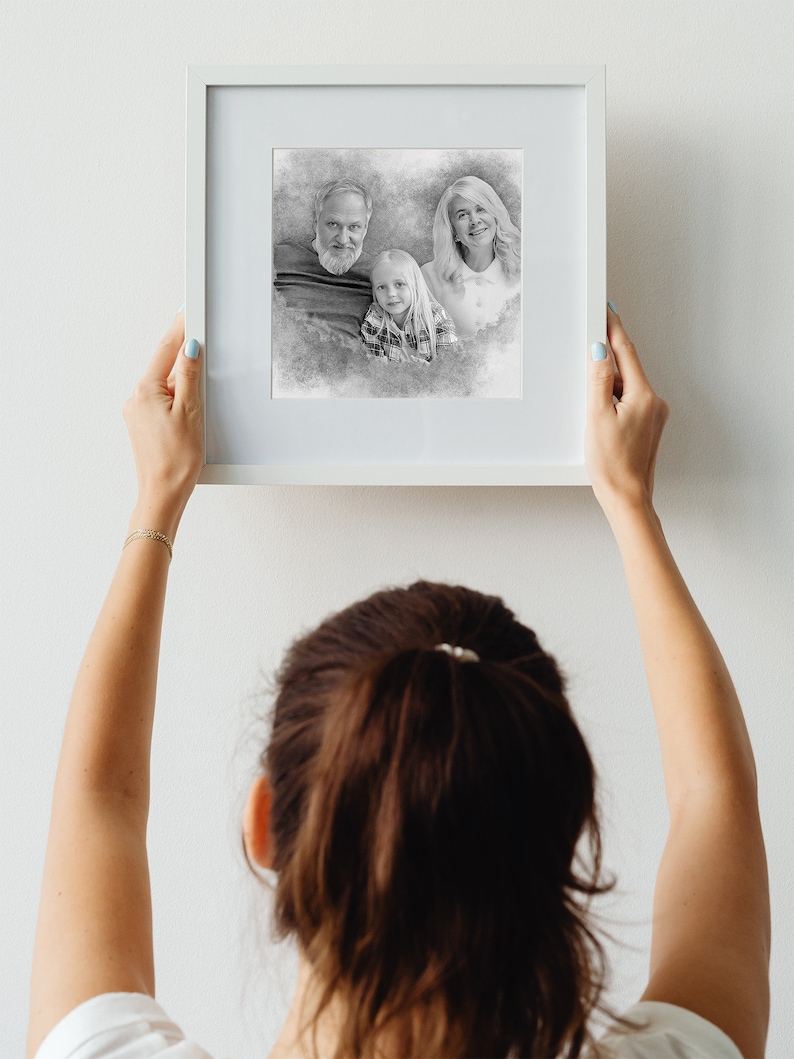 May include: A framed black and white pencil sketch of a family. The family consists of two adults and a child. The adults are standing behind the child, who is looking at the camera. The sketch is on a white background.