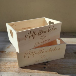 May include: Two wooden boxes with heart-shaped cutouts. The boxes are labeled "Notfallk&ouml;rbchen" and "Johannes & Lisa".