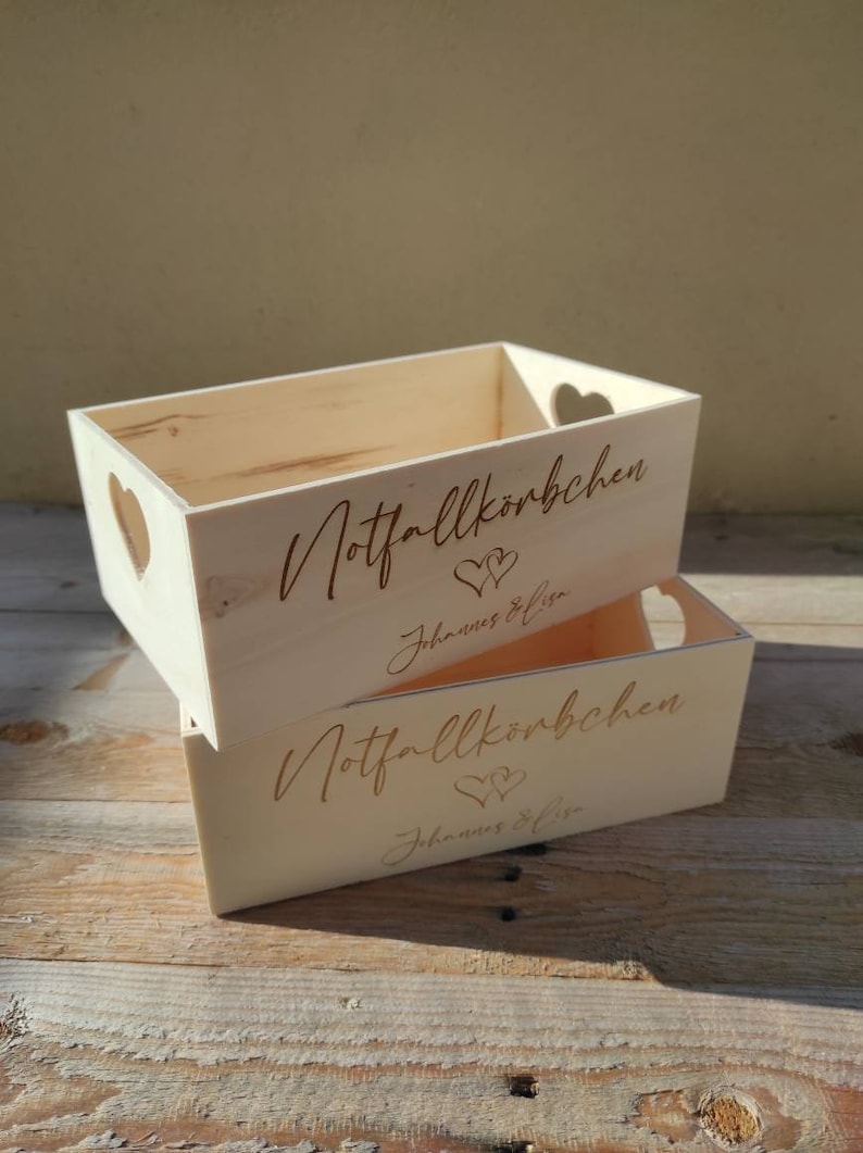 May include: Two wooden boxes with heart-shaped cutouts. The boxes are labeled "Notfallk&ouml;rbchen" and "Johannes & Lisa".