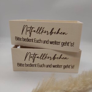 May include: Two wooden boxes with the text "Notfallk&ouml;rbchen Bitte bedient Euch und weiter geht's!"  engraved on the front.