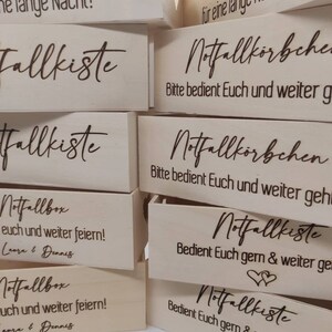 May include: A stack of wooden boxes with the text "Notfallkiste" and "Notfallbox" engraved on them. The boxes are decorated with hearts and the text "Bedient Euch gern & weiter geht's!"