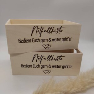 May include: Two wooden boxes with the text "Notfallkiste" and "Bedient Euch gern & weiter geht's!" engraved on them. The boxes are stacked on top of each other.
