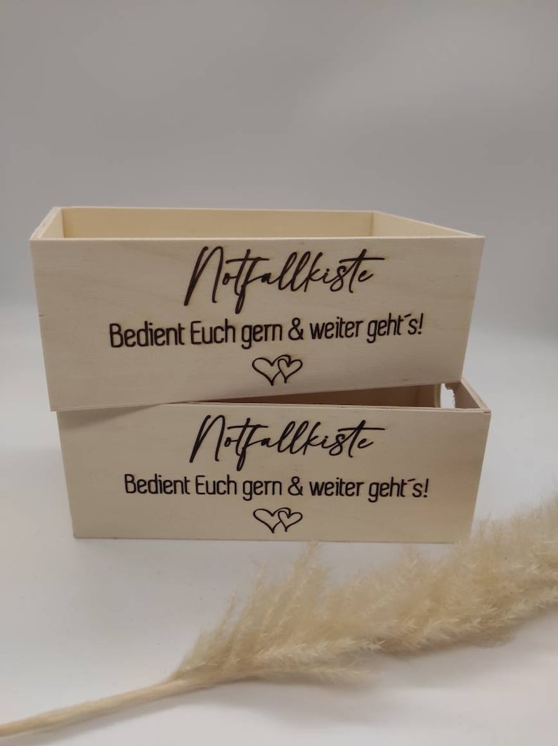 May include: Two wooden boxes with the text "Notfallkiste" and "Bedient Euch gern & weiter geht's!" engraved on them. The boxes are stacked on top of each other.
