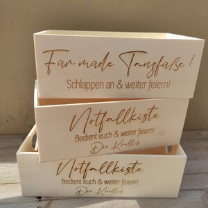 May include: Three wooden boxes stacked on top of each other. The top box says "For tired dance feet! Relax and keep partying!" The middle and bottom boxes say "Emergency kit. Help yourselves and keep partying! The Krollis"