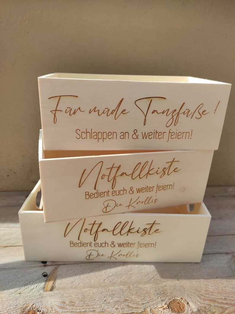 May include: Three wooden boxes stacked on top of each other. The top box says "For tired dance feet! Relax and keep partying!" The middle and bottom boxes say "Emergency kit. Help yourselves and keep partying! The Krollis"