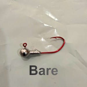May include: A silver fishing jig with a red hook. The jig has a round head and a small loop at the top. The word "Bare" is written below the jig.