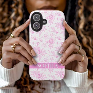 May include: A white phone case with a pink floral pattern and the name "Sophia" printed in pink on a pink stripe.