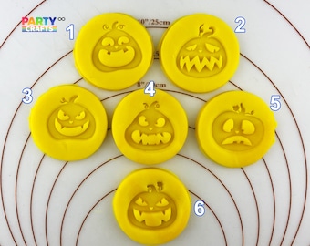 May include: Six yellow plastic pumpkin cookie cutters with different facial expressions. The cutters are arranged in a circle on a white surface with brown concentric circles.