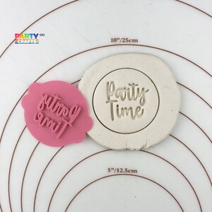 May include: Pink plastic cookie cutter with the words "Party Time" in a cursive font. The cutter is shown on a white surface with a 5 inch diameter circle marked around it.