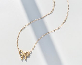 May include: A gold chain necklace with a delicate bow pendant.