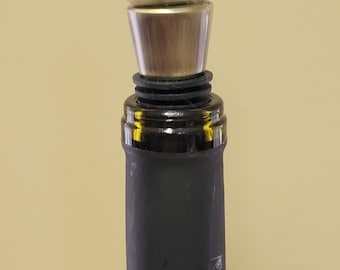 May include: A wine bottle stopper with a green and white stone top. The stopper is made of metal and has a black rubber seal.