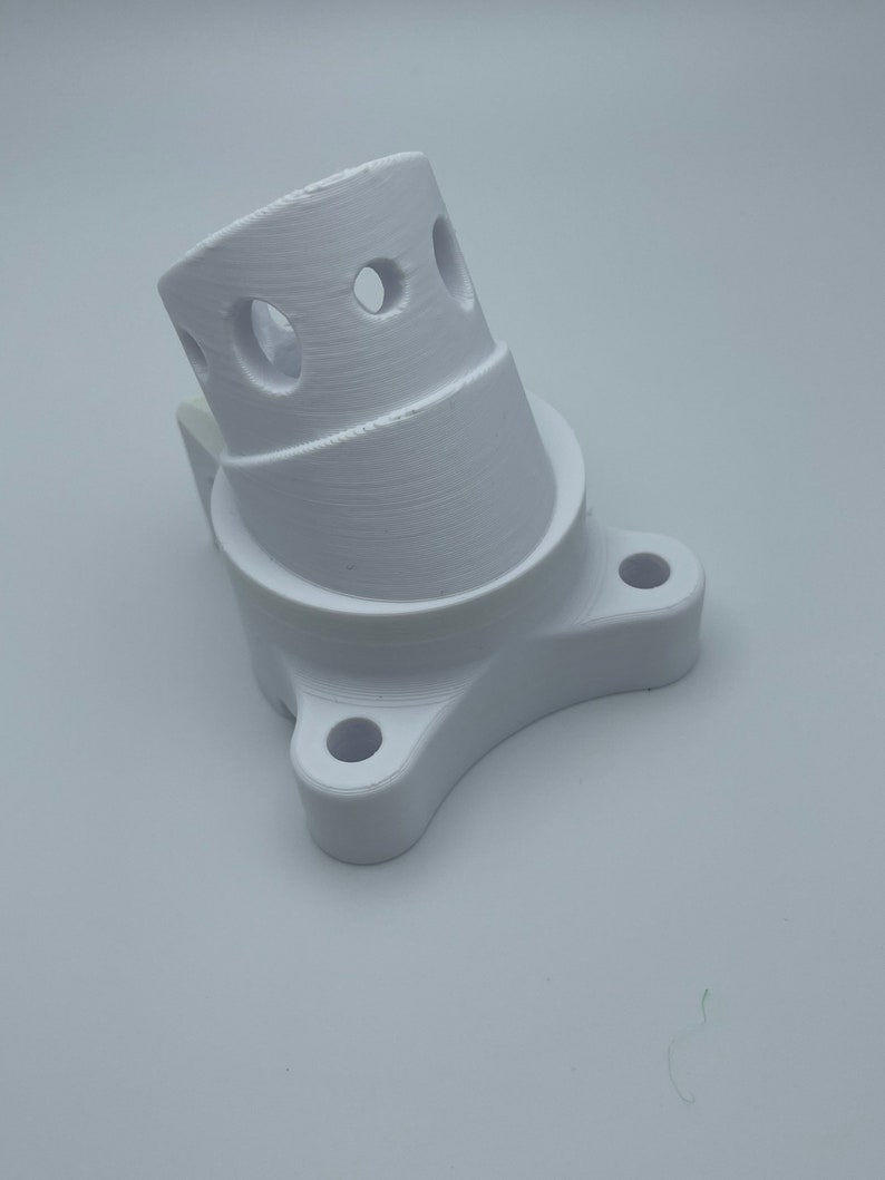 May include: White plastic 3D printed adapter with a round base and a curved top with four holes.