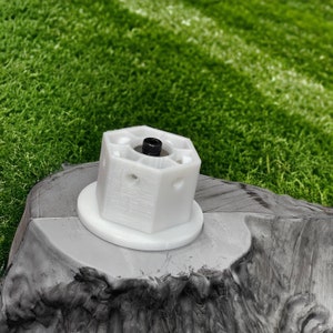 May include: White plastic hexagonal object with a black screw in the center, mounted on a gray surface.