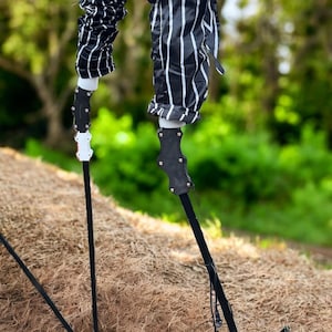 May include: Two black and white striped legs with black and white handles attached to the bottom. The legs are made of a fabric material and the handles are made of a hard plastic material. The legs are standing on a brown surface.