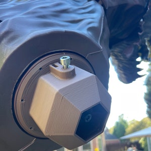 May include: A brown 3D printed camera mount with a hexagonal opening and a silver screw. The mount is attached to a larger brown object.