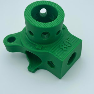 May include: Green 3D printed plastic part with a round opening and multiple holes. The part has the number "800" printed on it.