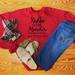 May include: A red sweatshirt with the text "Mystic Moon Socks Your Design Here" is paired with blue jeans, plaid gloves, and cream-colored shoes. A red rose and fern complete the ensemble, arranged on a wooden surface.