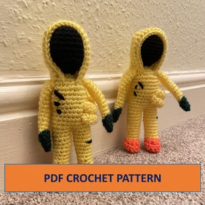 May include: Two crocheted yellow figures with black faces and green hands. The figures are wearing yellow hazmat suits. The text "PDF CROCHET PATTERN" is at the bottom of the image.