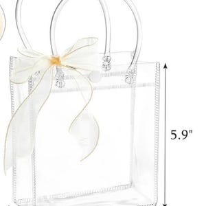 Puede incluir: Bolso tote transparente con un lazo de cinta blanco. El bolso tiene asas transparentes y mide 15 cm de alto, 12,5 cm de ancho y 7 cm de profundidad. El bolso est&aacute; hecho de un material transparente y tiene un lazo decorativo.