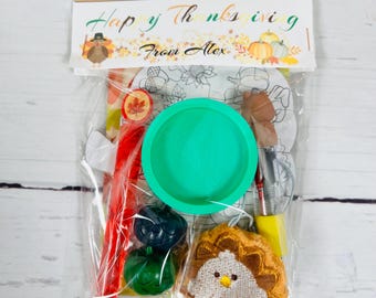 Puede incluir: Una bolsa transparente llena de artículos con temática de Acción de Gracias. La bolsa incluye un cuenco verde, un crayón rojo, un pequeño pavo bordado y una calabaza. La parte superior de la bolsa dice "Happy Thanksgiving From Alex."