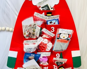 Op de afbeelding: Een rode vilt kerst-adventskalender in de vorm van Sinterklaas met 24 vakjes. Elk vakje bevat een klein cadeautje, zoals stickers, speelgoed en andere feestelijke items. De kalender is versierd met wit vilt voor de baard en de muts van Sinterklaas, en met groen vilt voor de rand van zijn muts.