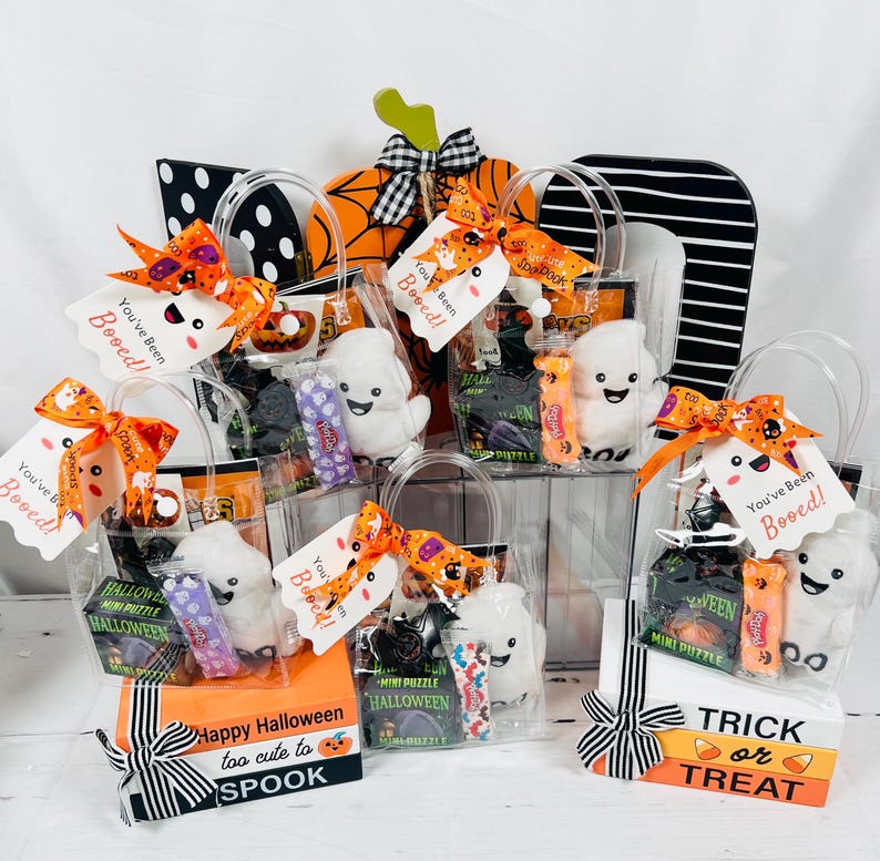 Puede incluir: Varias bolsas de regalo con tem&aacute;tica de Halloween llenas de golosinas y peque&ntilde;os juguetes. Cada bolsa incluye un fantasma de peluche, caramelos y una etiqueta que dice "You've Been Booed!". Las bolsas est&aacute;n decoradas con cintas naranjas y negras.
