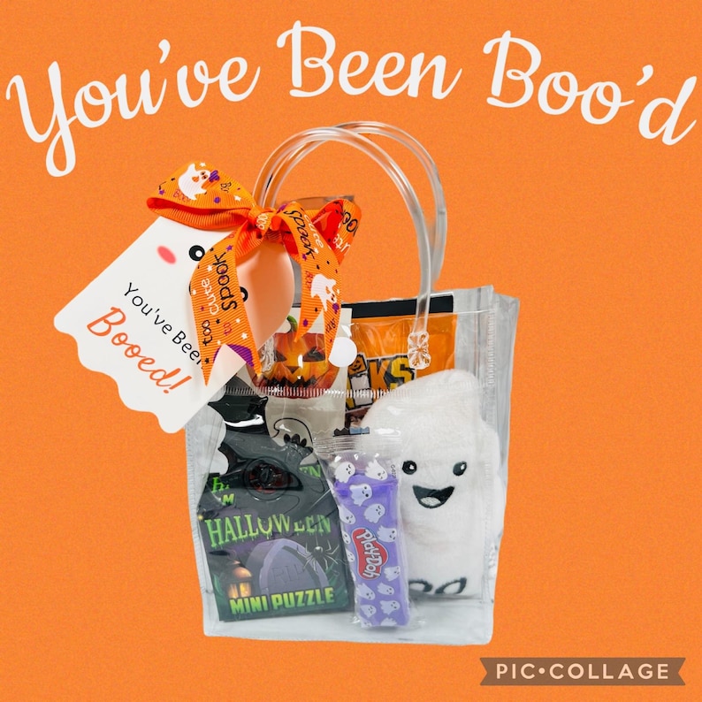 Puede incluir: Una bolsa transparente llena de golosinas y juguetes de Halloween. La bolsa incluye un fantasma de peluche, un mini rompecabezas, Play-Doh y caramelos. Una etiqueta con el texto "You've Been Boo'd!" est&aacute; adjunta.