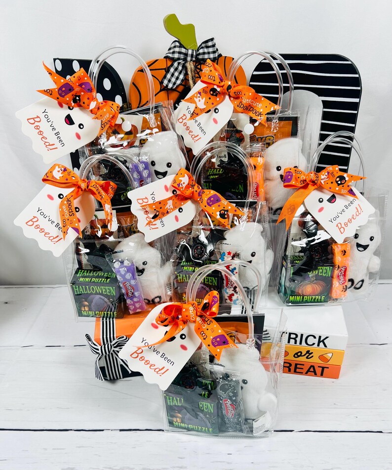 Puede incluir: Bolsas de regalo tem&aacute;ticas de Halloween llenas de golosinas y juguetes. Cada bolsa transparente contiene un peluche de fantasma blanco, caramelos y un mini rompecabezas. Las bolsas est&aacute;n adornadas con lazos naranjas y negros y la etiqueta "You've Been Booed!"