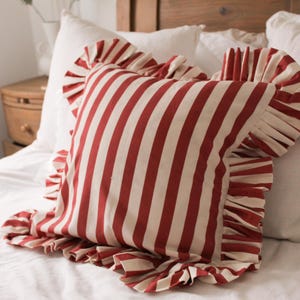 May include: A red and white striped pillow with a ruffled edge. The pillow is made of a soft, cotton fabric and is perfect for adding a touch of farmhouse style to any room.