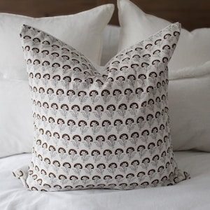 May include: A white pillow with a brown floral pattern on a white bed.