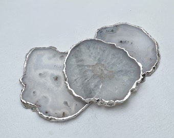 May include: Three white agate coasters with silver trim. The coasters are stacked on top of each other.