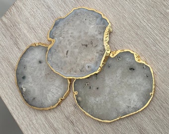 May include: Three gray agate coasters with gold trim. The coasters are round and have a natural, organic shape.